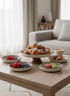 Dessert display on a coffee table with pastries, macarons, and fruit in a living room setting.
