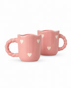Two pink ceramic mugs with scalloped handles and small white heart details, shown on a clean white background.