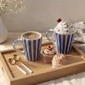 Cup of coffee with a striped mug, cupcakes, and spoons on a wooden tray.