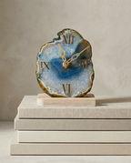 Decorative clock with agate-like design on a stack of books against a beige background