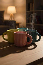 Four colorful mugs on a wooden surface with steam rising, in a warm indoor setting.
