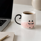 Cat-shaped mug with black handle on a desk next to a laptop