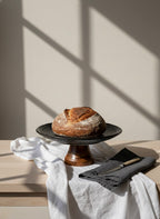 Loaf of bread on a black plate with a white cloth and knife in the background