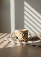 Ceramic mug with floral design on a light surface, casting shadows.