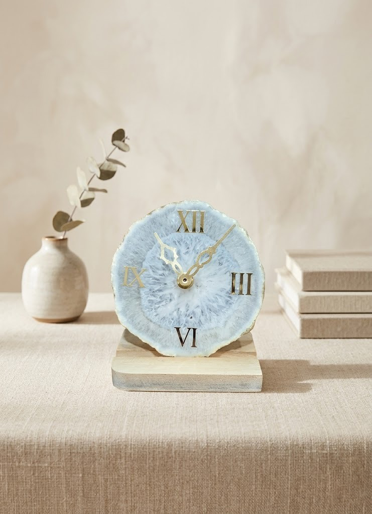 Decorative clock with Roman numeral design on a wooden base, placed on a surface with a neutral background.