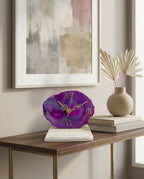 Purple clock on a wooden table with abstract art and decor in the background
