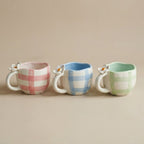 Three ceramic mugs with plaid patterns on a beige background