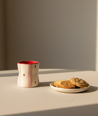 Ceramic mug with red interior and heart designs on a beige surface with cookies.