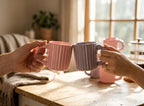 Two people holding pink mugs on a wooden table with a blurred background