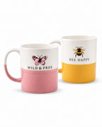 Two ceramic mugs on a white background. The front mug is white on top and pink on the bottom, with a pink butterfly graphic and the words 'WILD & FREE'.