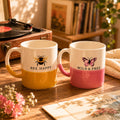 Two mugs with animal-themed designs and text on a wooden surface.