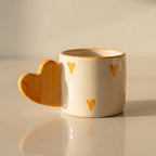 Ceramic mug with heart-shaped handle and heart designs on a beige background