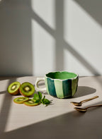 Green ceramic mug with kiwi slices and a sprig of mint on a wooden surface.