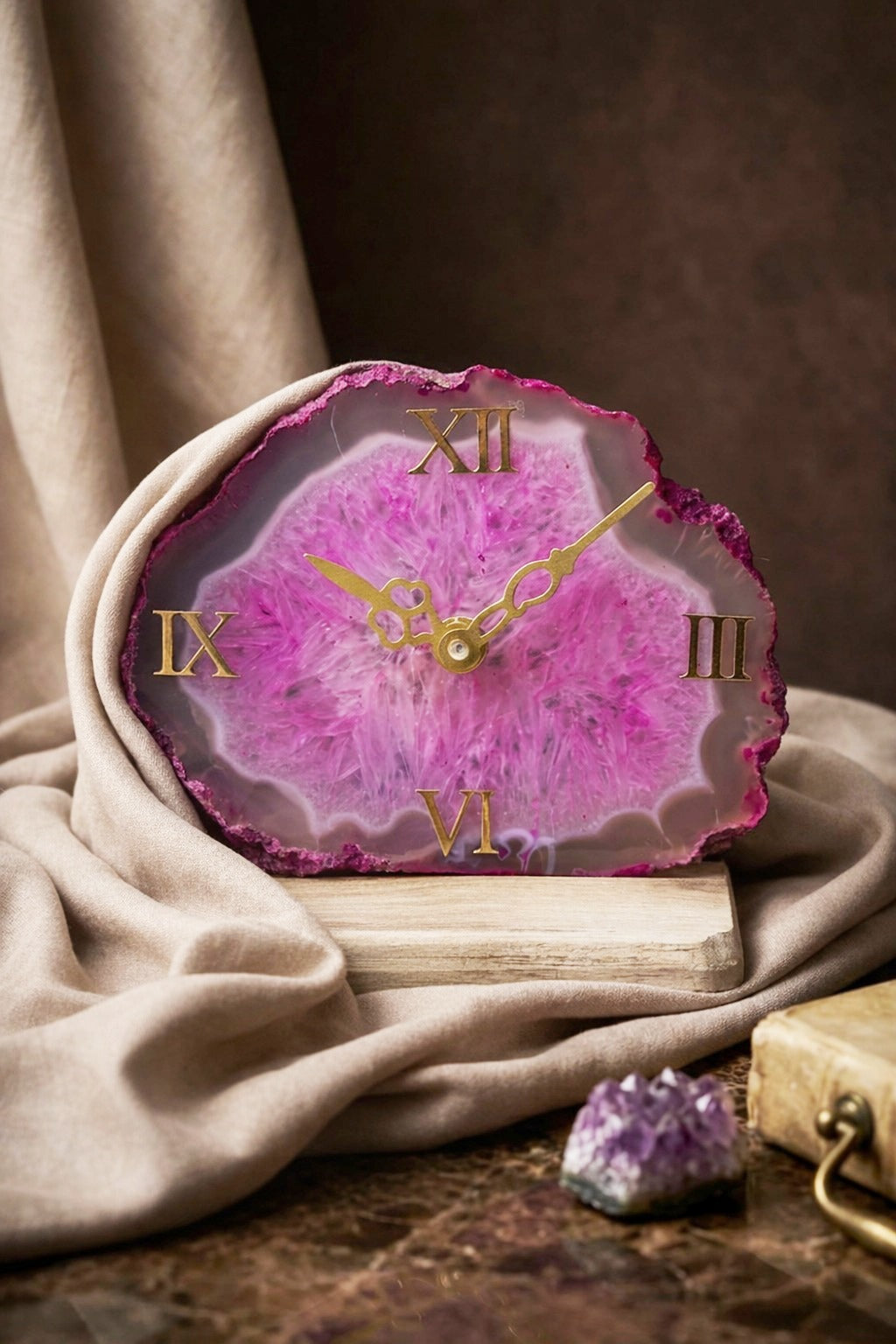Pink agate clock with gold Roman numerals on a textured surface