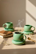 Three green ceramic mugs on a wooden surface with steam rising from one of them.