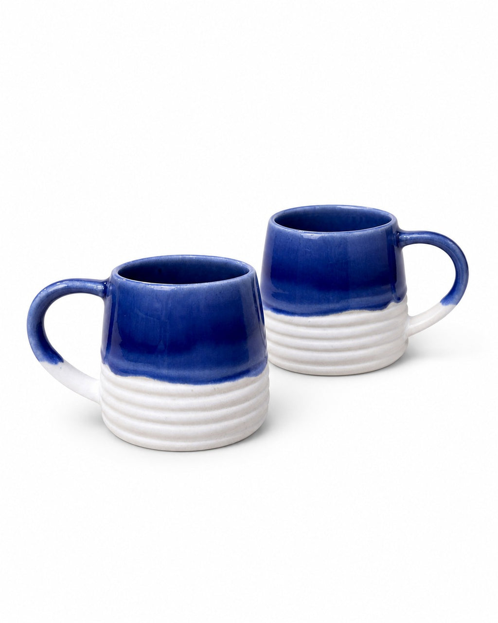 Two ceramic mugs with a glossy cobalt blue top half and a white ribbed bottom half, shown on a clean white background.