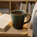 Steaming mug of coffee on a wooden table next to an open book