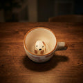 Small dog figurine inside a ceramic cup on a wooden surface