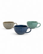 Three ribbed ceramic cups in beige, deep blue, and mint green, arranged on a clean white background.