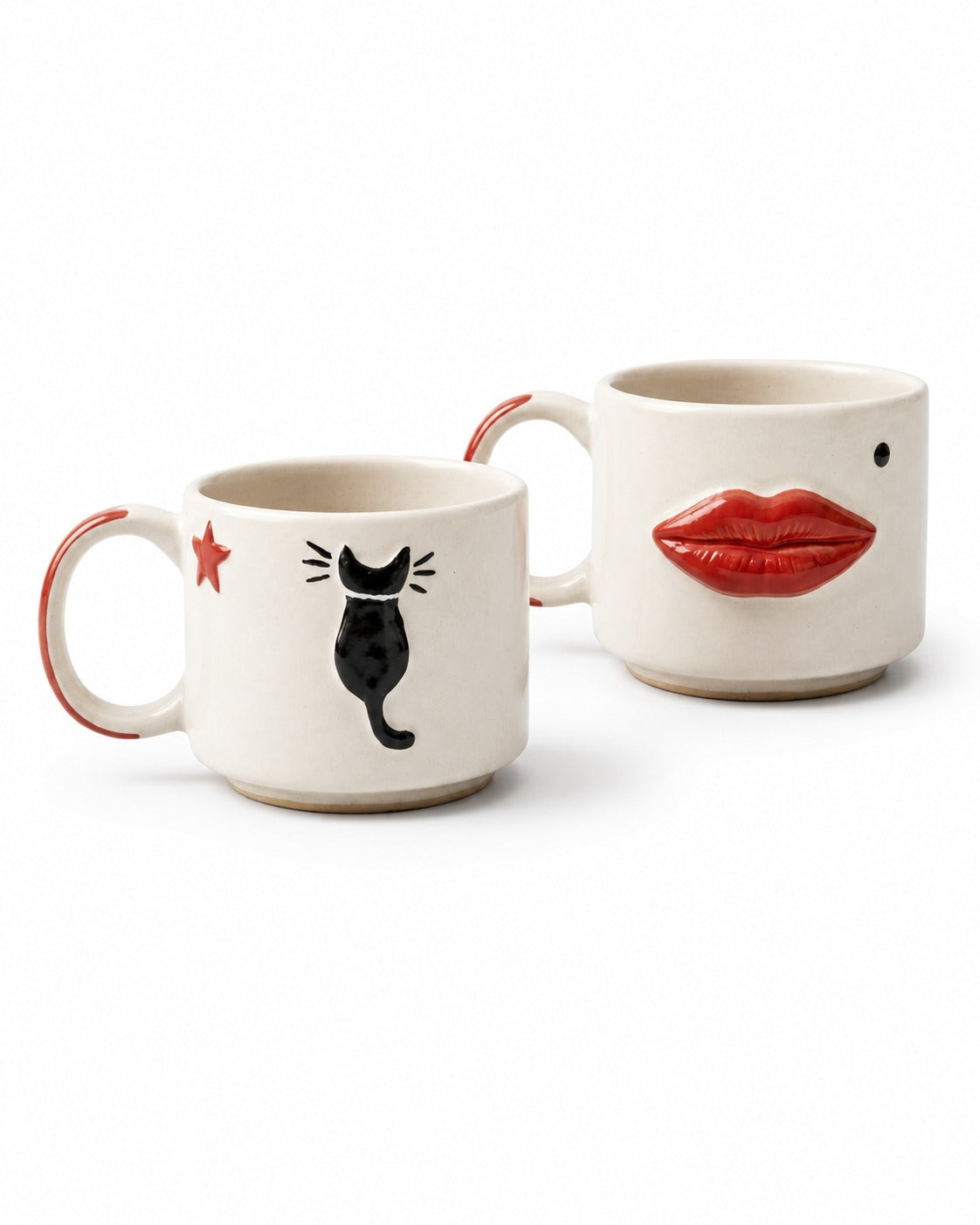 Two ceramic mugs on a white background. The front mug is cream-colored with a black cat silhouette, a small red star, and a red star outline on the handle.