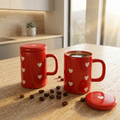 Two red mugs with heart designs on a kitchen counter with coffee beans.