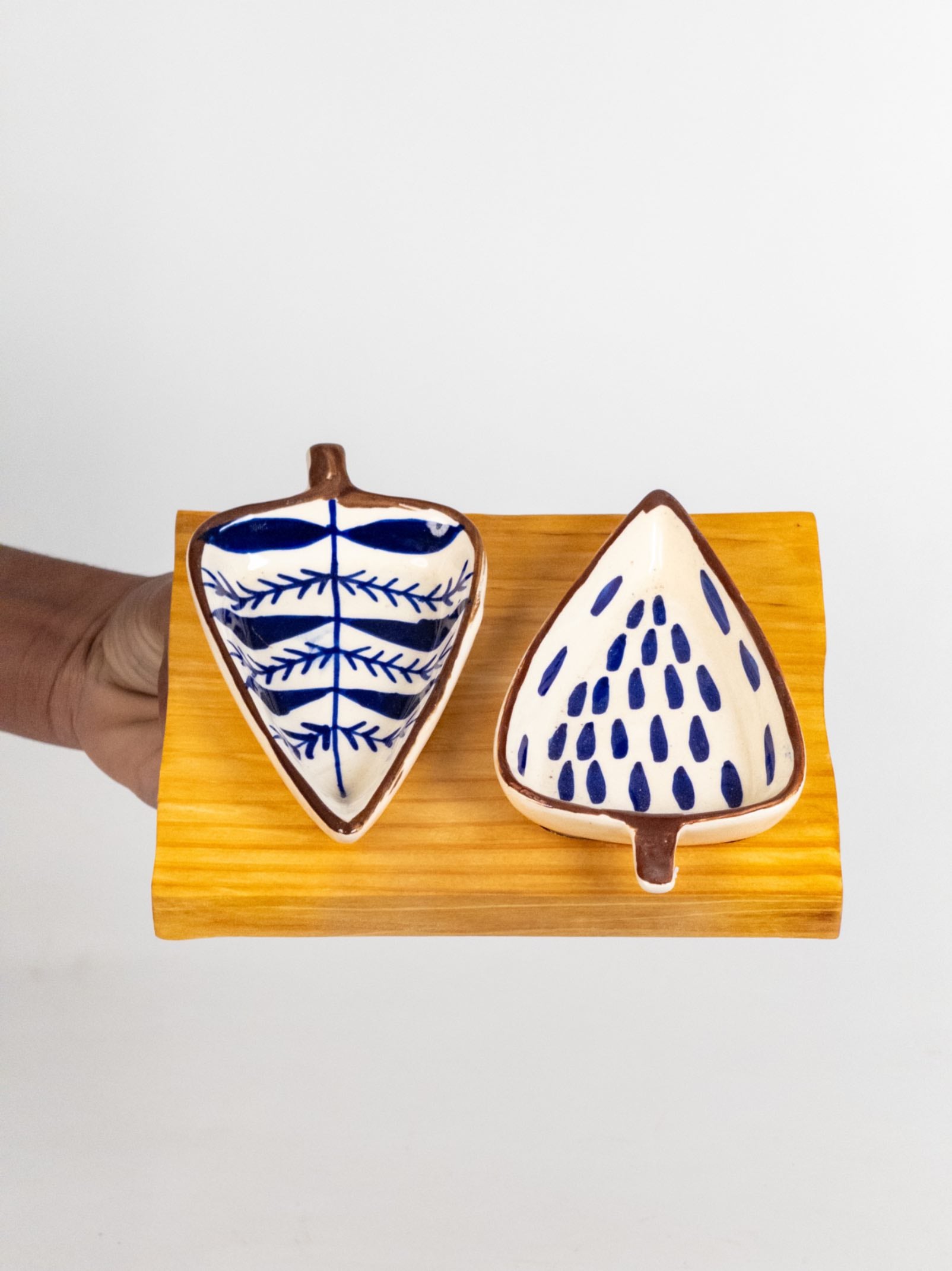Two ceramic leaf-shaped plates with blue patterns on a wooden stand against a white background