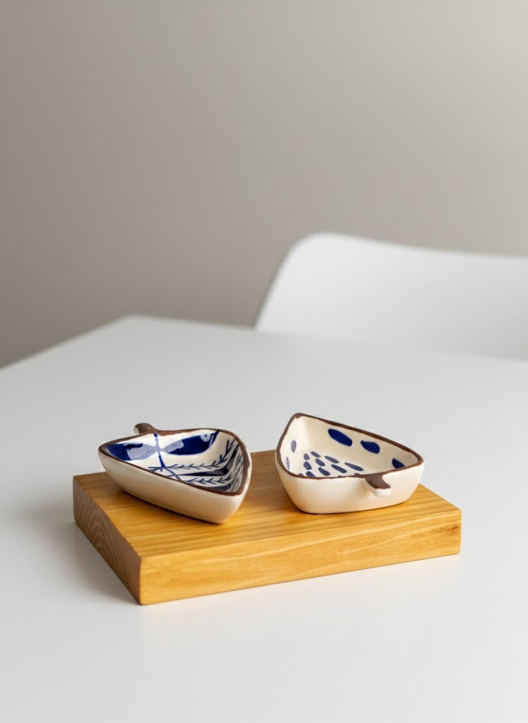 Two small ceramic bowls with blue patterns on a wooden stand against a neutral background