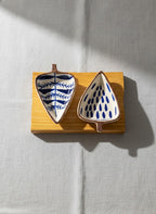 Two ceramic leaf-shaped bowls with blue patterns on a wooden stand against a light gray background
