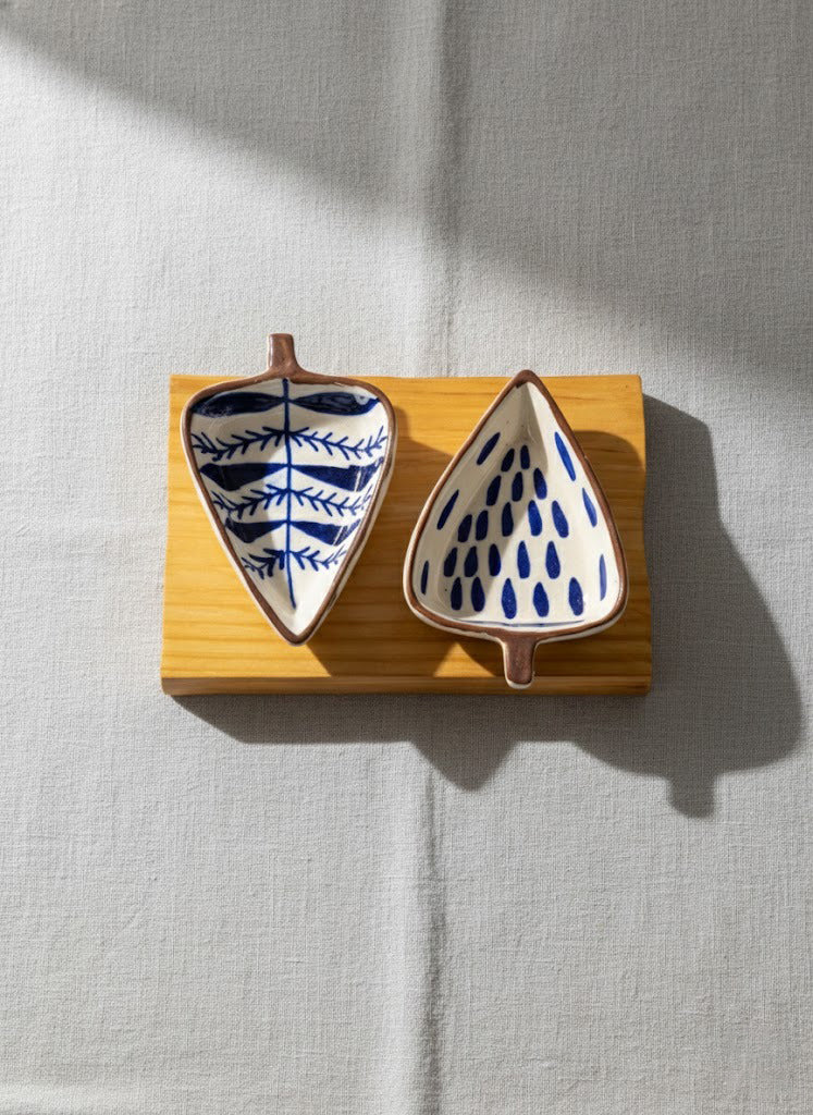 Two ceramic leaf-shaped bowls with blue patterns on a wooden stand against a light gray background