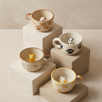 Four ceramic cups with animal-themed decorations on a beige surface