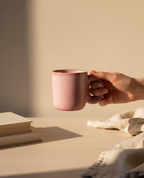 Hand holding a pink mug on a light wooden surface with a soft beige background