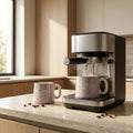 Espresso machine pouring coffee into a speckled mug on a wooden countertop.