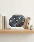 Decorative clock with Roman numeral design on a shelf with books and a plant.