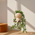 Decorative plant holder shaped like a smiling face with green leaves, hanging against a neutral wall.