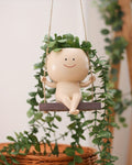 Decorative baby figurine with a leafy head on a swing surrounded by greenery.