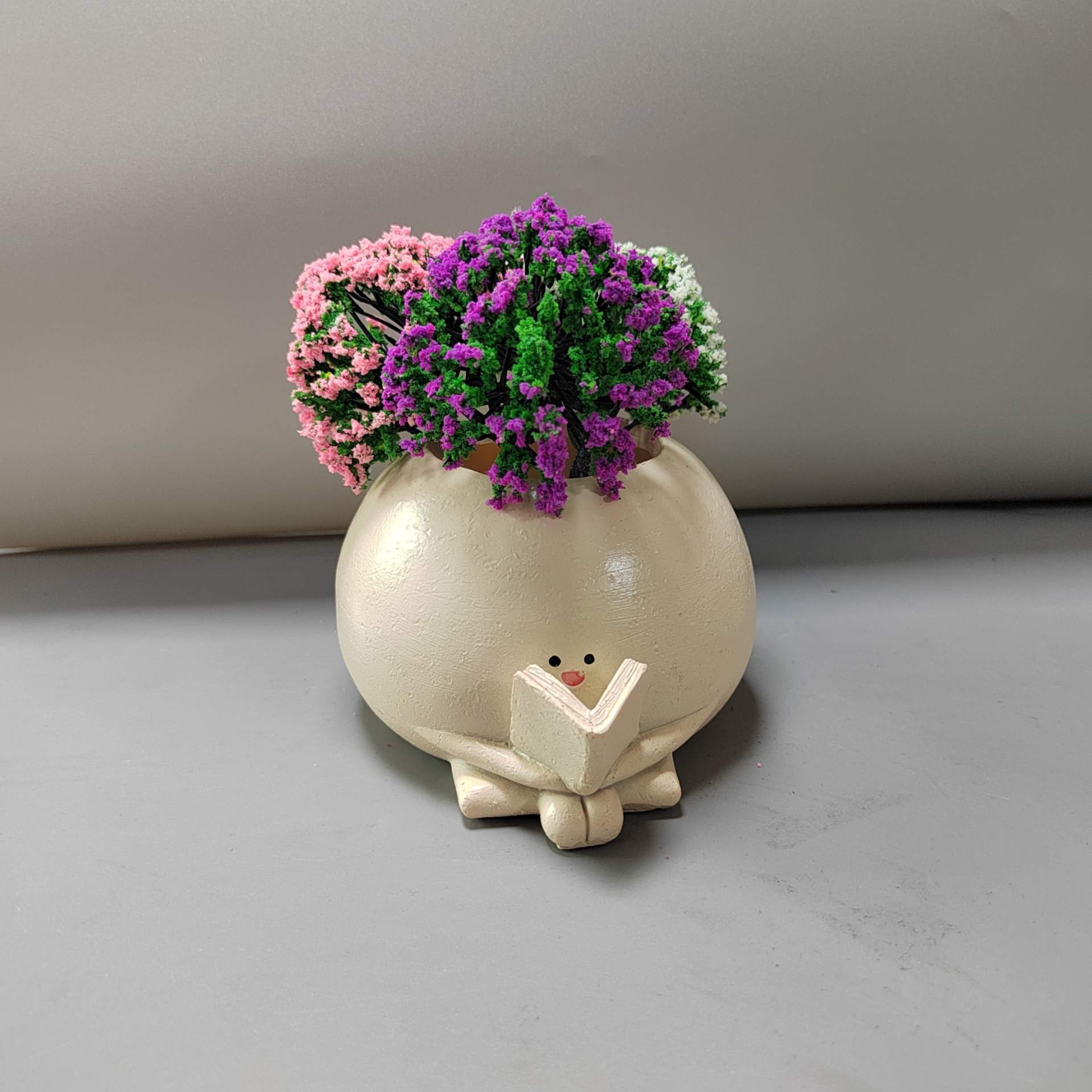 Ceramic planter with cartoon face and flowers on a neutral background