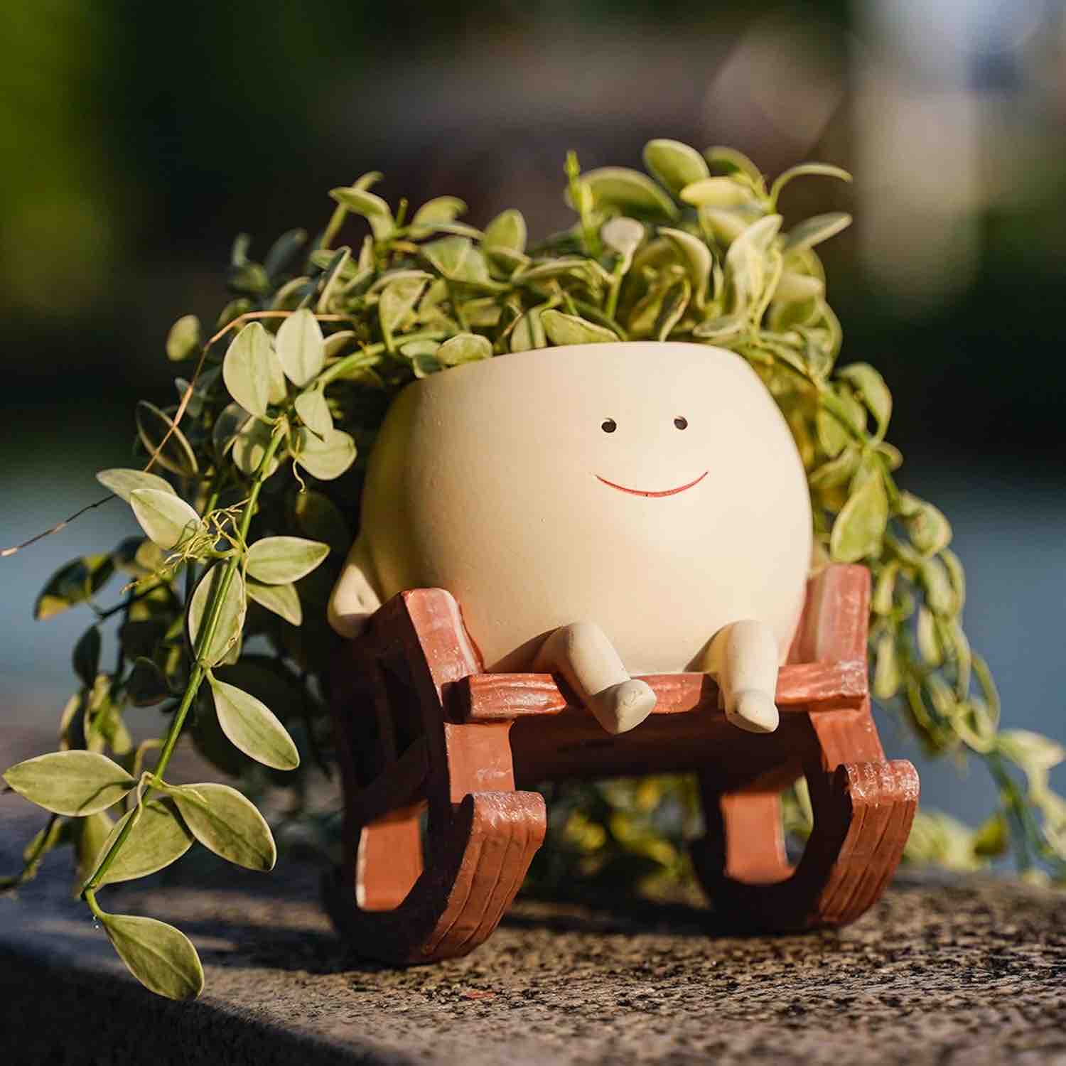 Ceramic planter with a smiling face on a wooden bench surrounded by green leaves.