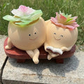Two smiling ceramic plants with flowers on a stone surface