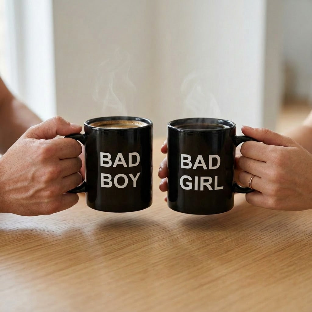 Two black mugs labeled 'BAD BOY' and 'BAD GIRL' held by two people on a wooden surface.
