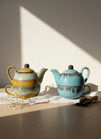 Two ceramic teapots and cups on a table with sunlight casting shadows.