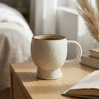 Speckled ceramic mug on a wooden surface with books and decor in the background