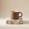 Pink mug with yellow interior on a stone surface against a beige background