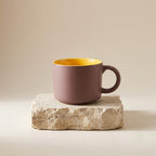 Pink mug with yellow interior on a stone surface against a beige background