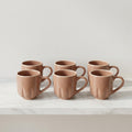 Set of six terracotta mugs on a light surface with a neutral background