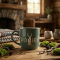 Green mug with 'Wild & Free' and deer design on a wooden table with natural elements.