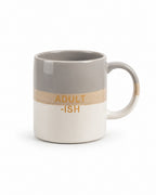A ceramic coffee mug with a horizontal color-blocked design featuring a gray top half, a textured beige middle band with the text 'ADULT -ISH' in gold, and a white bottom half.