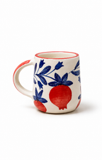 A white ceramic mug featuring a blue floral pattern and red pomegranate motifs, with a red handle and rim, shown on a white background.