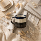 Ceramic mug with black and white design on a textured surface with dried plants and a book.