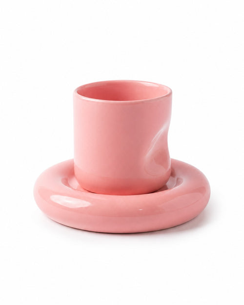 A glossy pink ceramic cup with a wavy, sculptural design, resting on a matching round saucer against a clean white background.