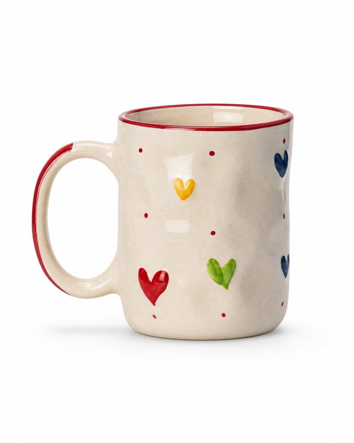An off-white ceramic mug with a red rim and handle accent, decorated with hand-painted colorful hearts in red, green, yellow, and blue, set against a plain white background.
